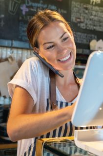 Waitress talking on the phone at a restaurant taking a delivery order and looking happy - food service concepts